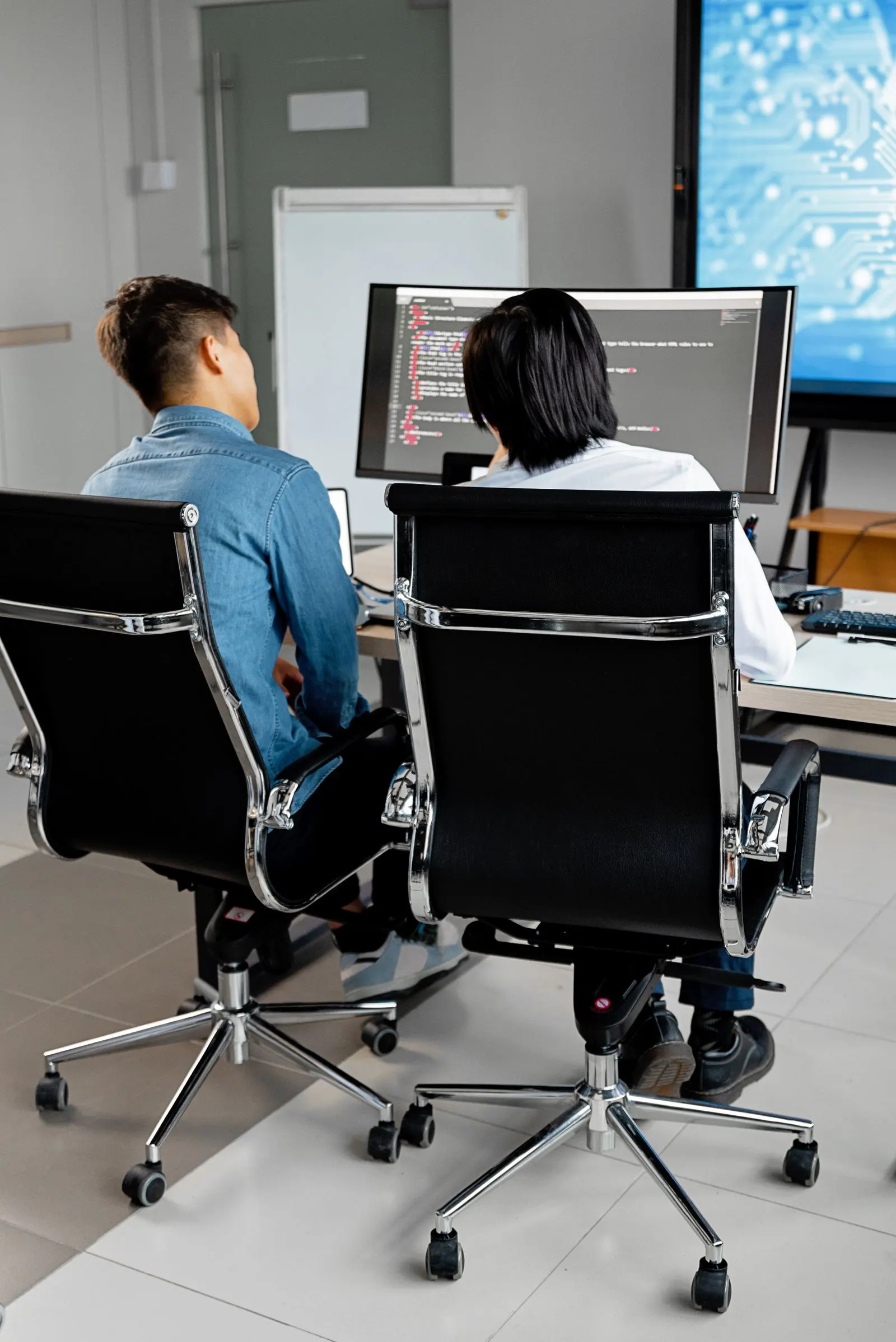 Two people reviewing work on dual monitors